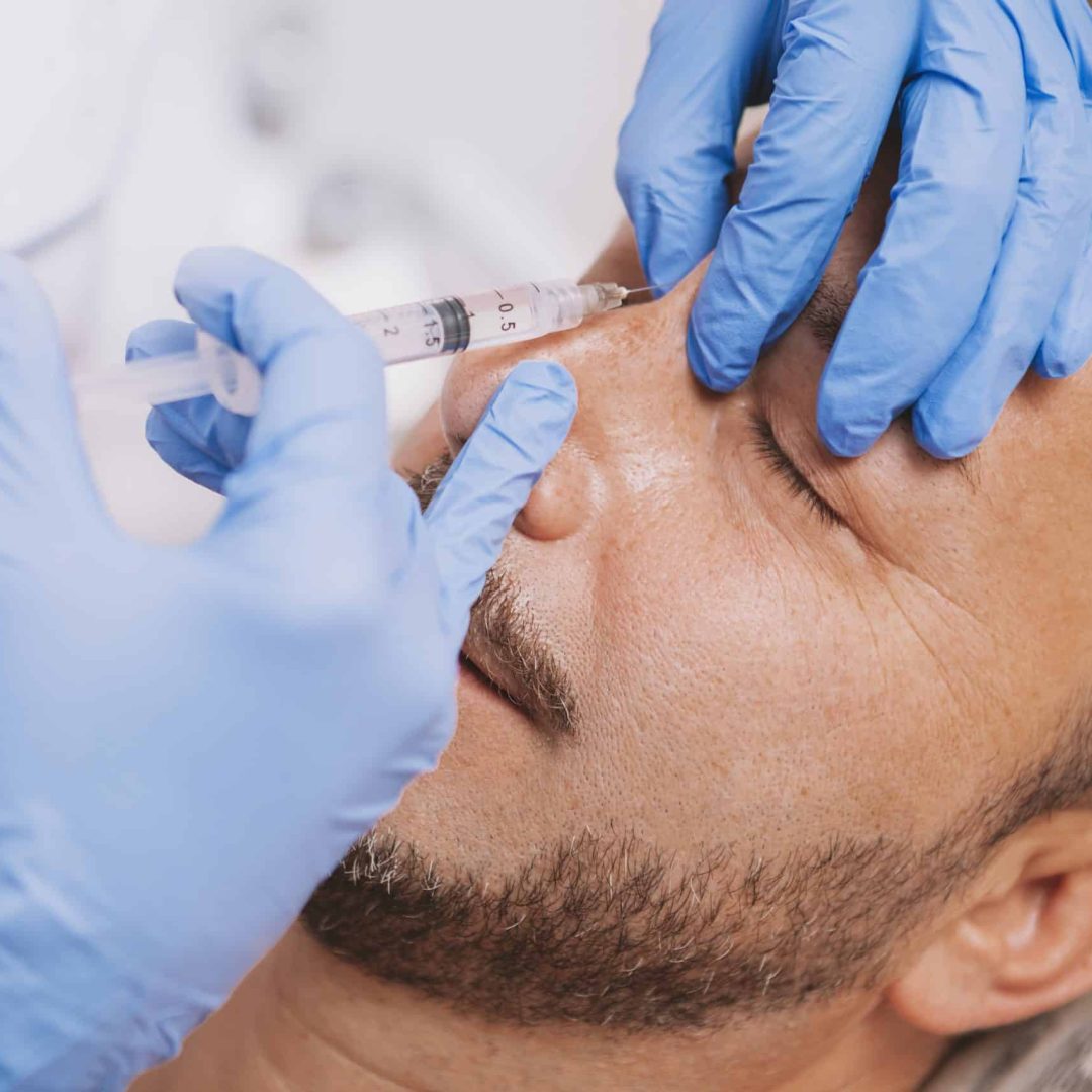 Cropped close up shot of a professional beautician performing non surgical nose job on a mature male client. Bearded man getting non-surgical nose job by rofessional cosmetologist
