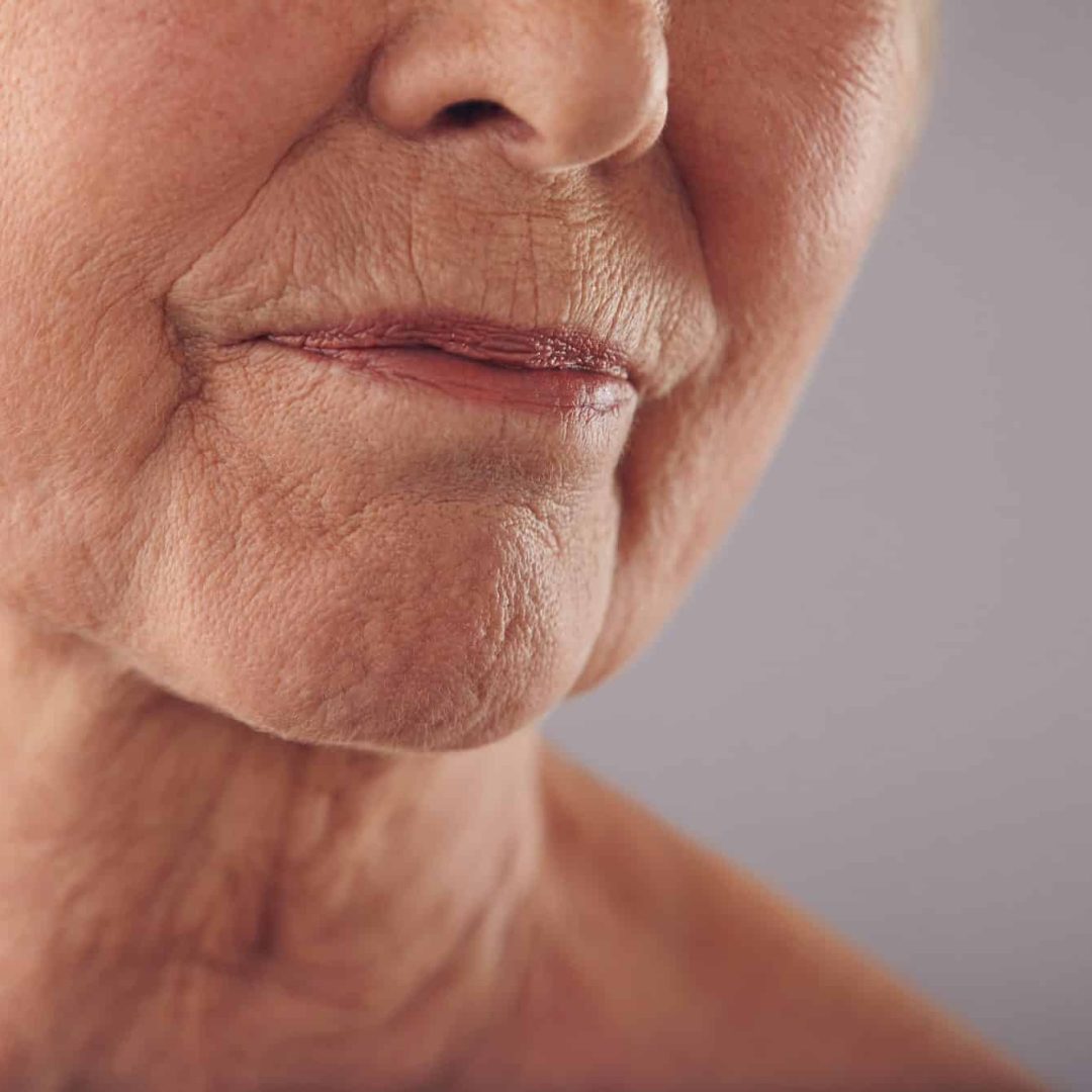 Senior female face with wrinkled skin Macro of a senior female face with wrinkled skin against grey background. Cropped old woman face.