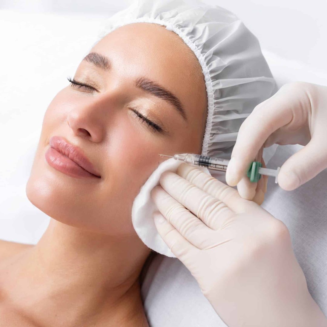 Beautiful relaxed woman at beautician cabinet receiving anti wrinkle injections on cheekbones, lying with closed eyes in beauty salon Beautiful relaxed woman at beautician cabinet receiving anti wrinkle injections on cheekbones, lying with closed eyes in beauty salon